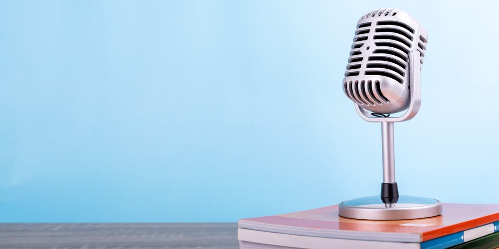 Retro microphone with many book put on wooden table isolated on blue background.
