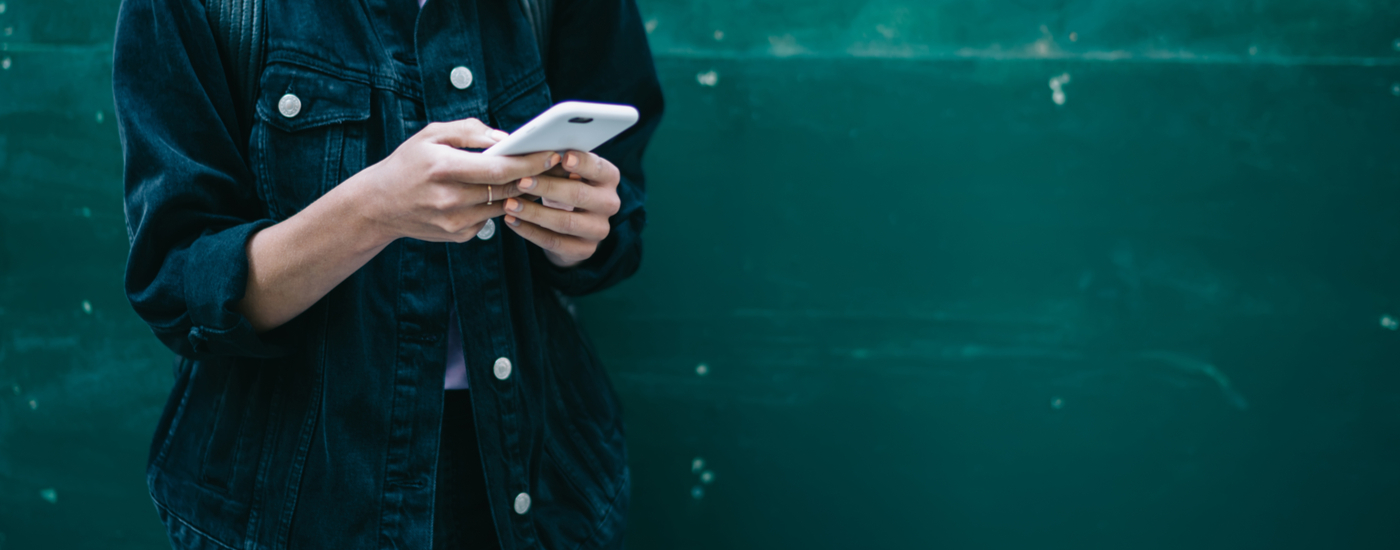 Woman in black denim jacket looks down at smartphone
