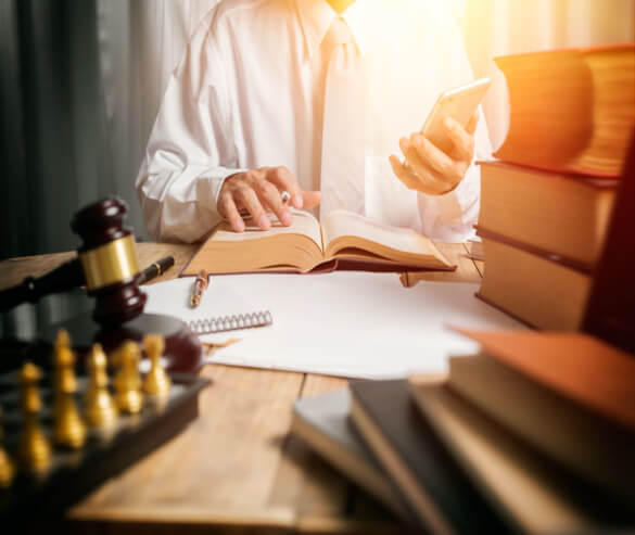 a lawyer shown looking at a smartphone while reading a law book at his desk